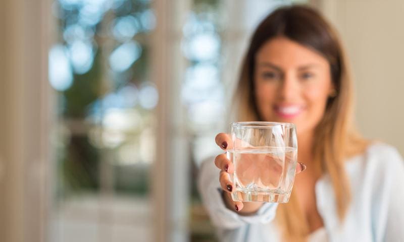 Happy woman offering up a glass of water